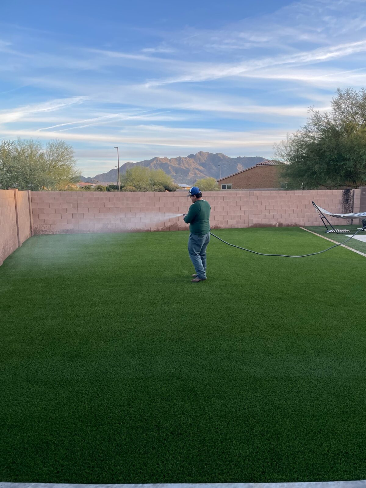 A man hoses down a synthetic grass backyard.