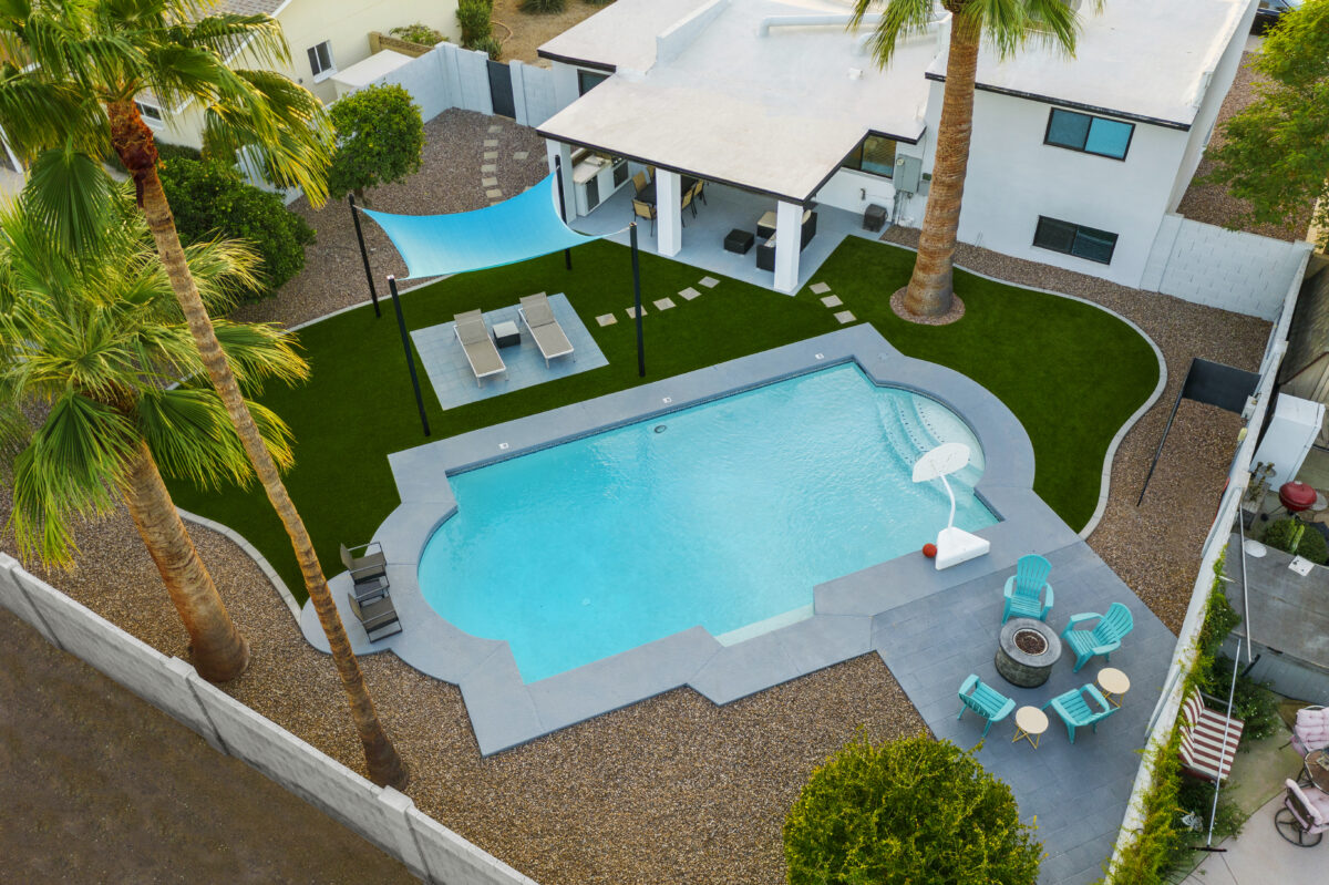 A modern backyard in East Valley, Arizona, with desert landscaping, including lush synthetic grass installation next to a swimming pool and fire pit. Project by Alpine Turf.