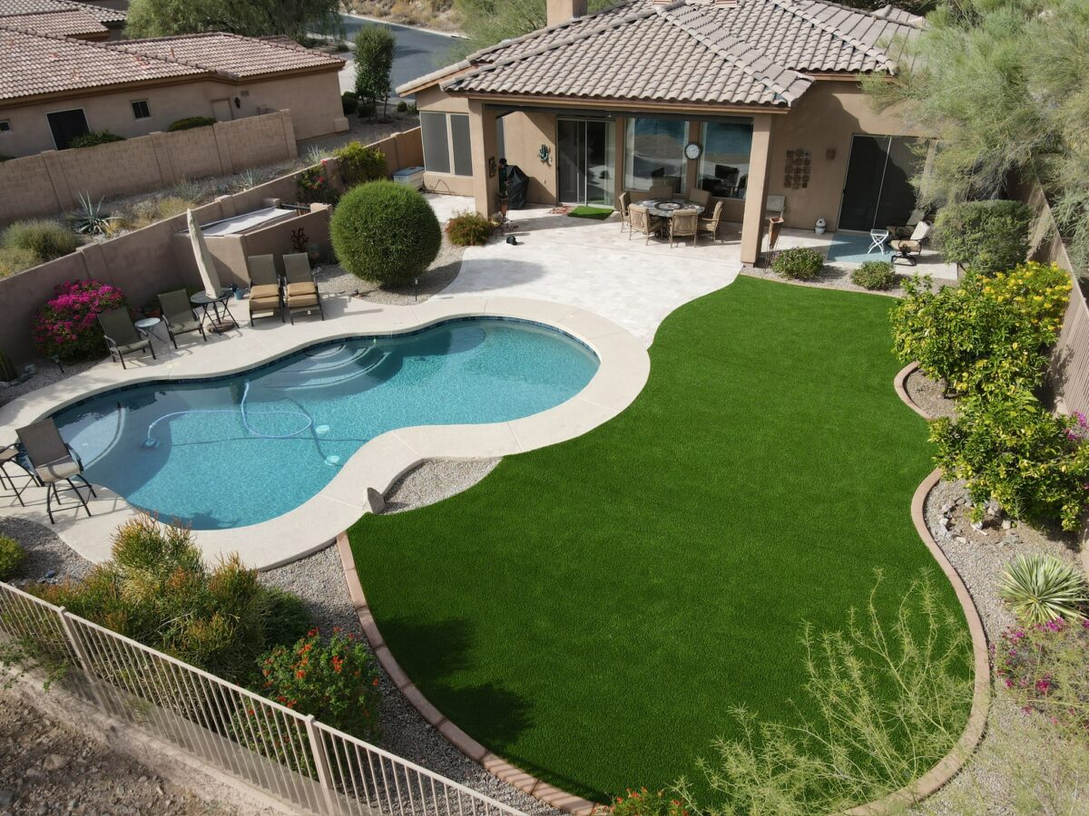 A synthetic grass lawn next to a freeform swimming pool in a small backyard in East Valley, Arizona. Installation by Alpine Turf.