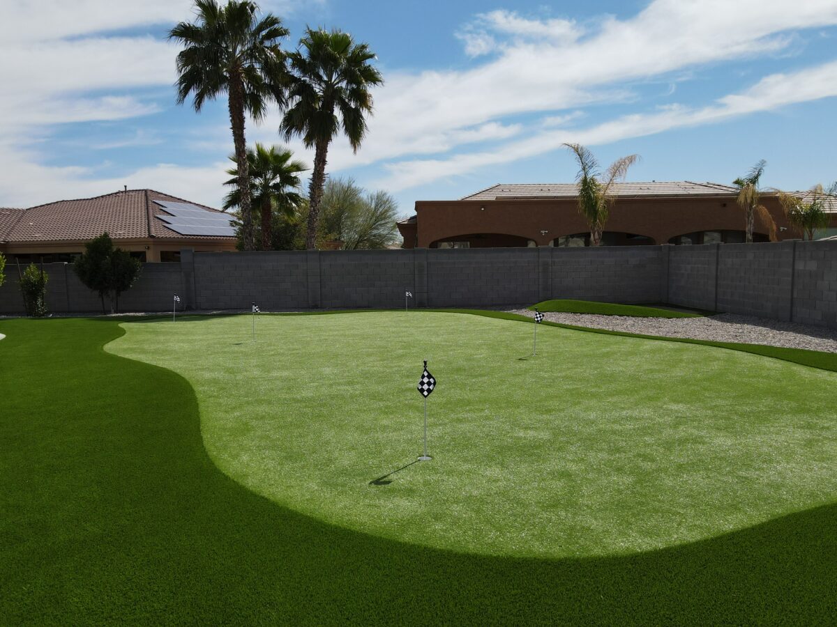 A turf putting green with a corner sand trap in a residential backyard.
